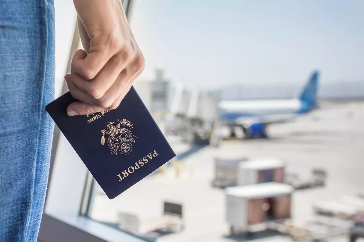 na foto vemos a mão de uma mulher segurar um passaporte enquanto ela espera em uma sla de embarque. Ela está viajando para obter ideias novas para inovas as empresas de turismo do mercado brasileiro