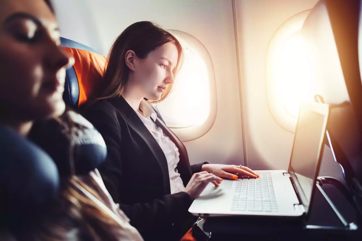 Empresária trabalhando no laptop sentado perto da janela em um avião. Internet a bordo durante os voos