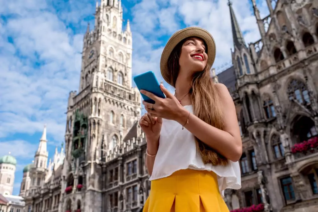 Jovem turista usando telefone celular na praça central em frente ao famoso prédio da prefeitura em Munique. Agora o perfil do turista mudou, fique atento às tendências.